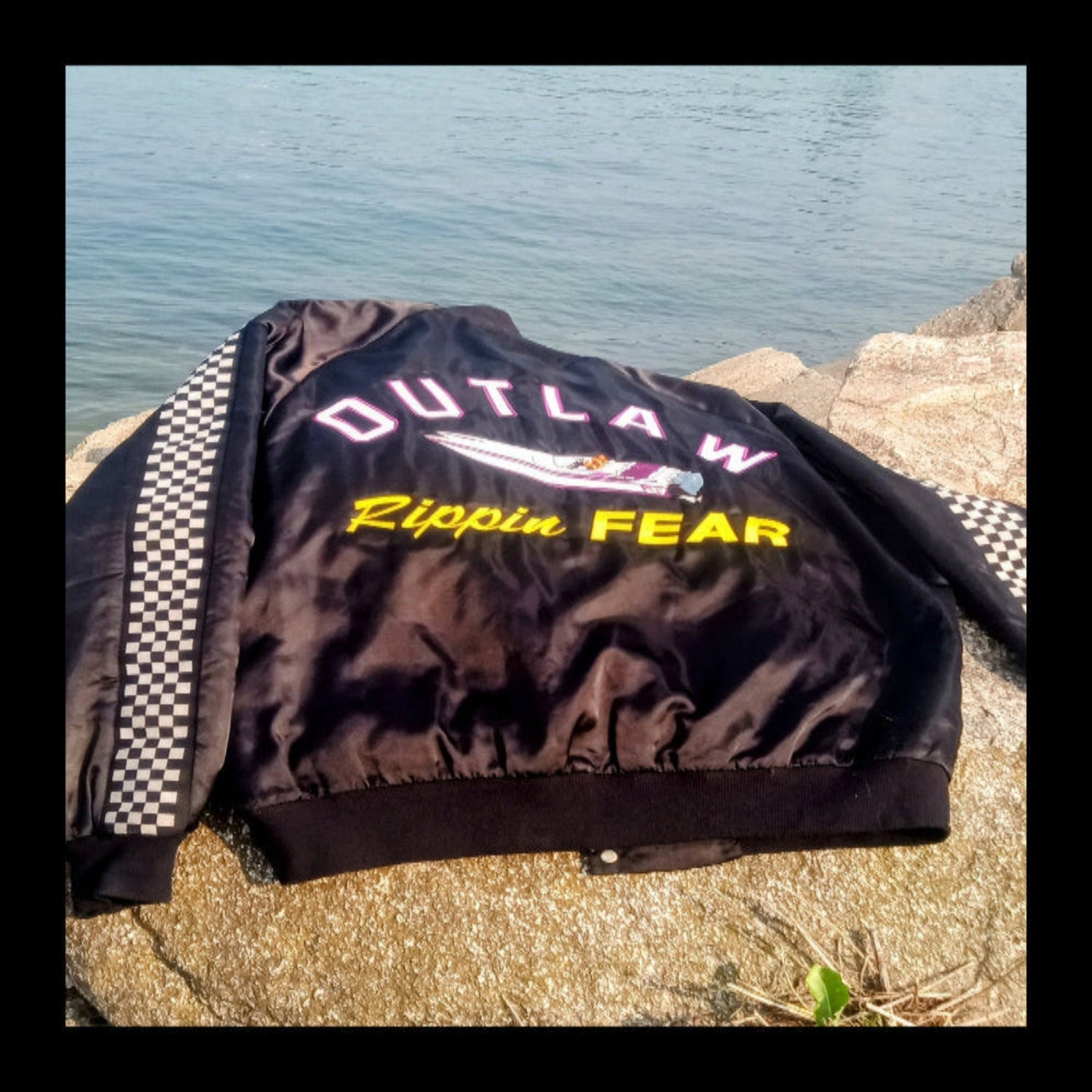 Black jacket with 'Outlaw Rippin Fear' text on a rocky surface near water